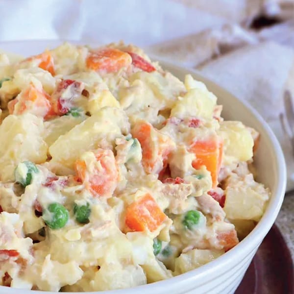 A white bowl filled with creamy Russian salad, featuring potatoes, carrots, and peas.