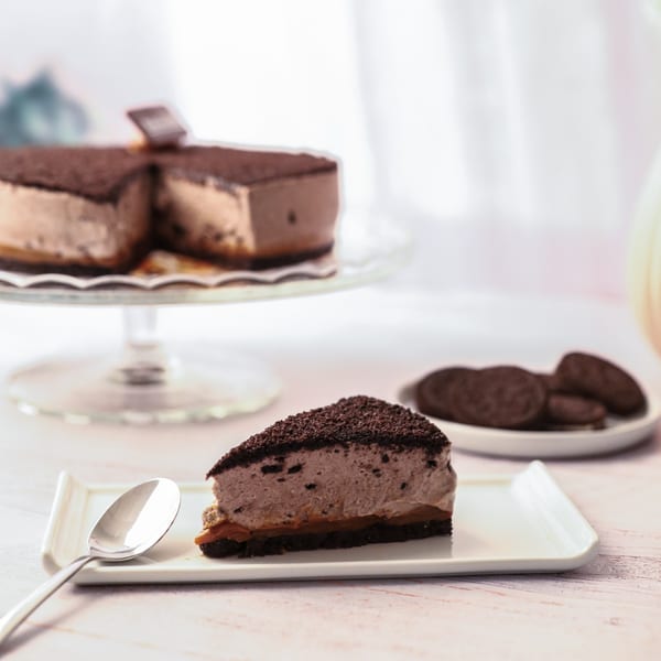 A slice of chocolate mousse cake with dulce de leche and a whole cake in the background.