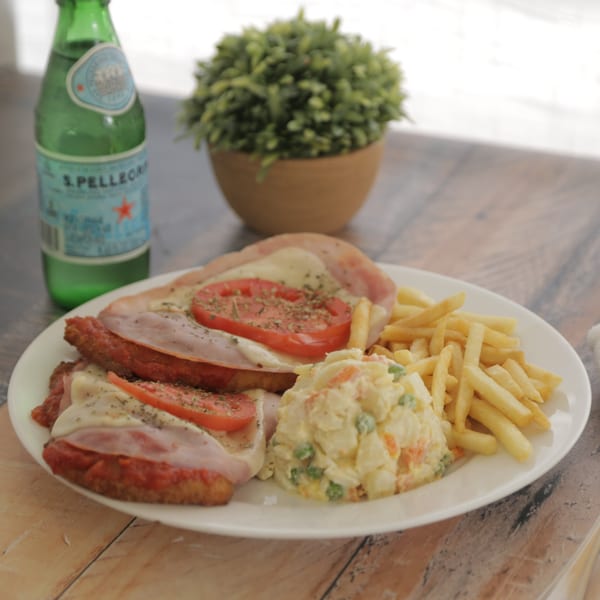 Argentinian milanesa with ham, cheese, and tomato, served with fries and potato salad.