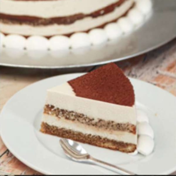 A slice of tiramisu cake with cocoa powder on top, served on a white plate with a spoon.