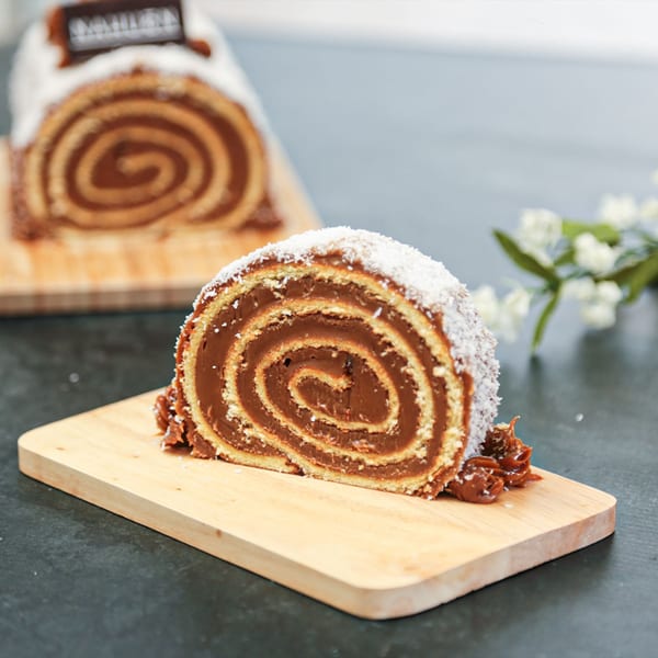 A slice of Argentinian pionono cake with dulce de leche filling and shredded coconut on a wooden board.