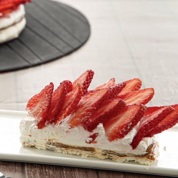 A slice of Argentinian strawberry and cream cake on a white rectangular plate.