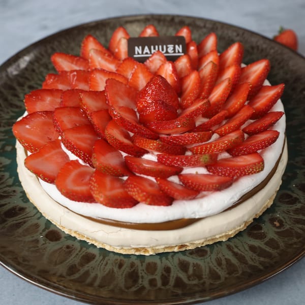 A Nahuen strawberry cake with white cream and dulce de leche on a dark plate.