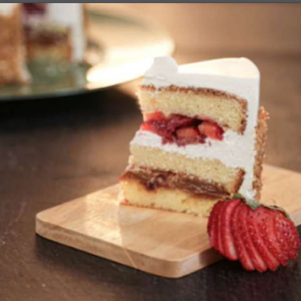 Slice of strawberry and dulce de leche cake with white frosting on a wooden board.