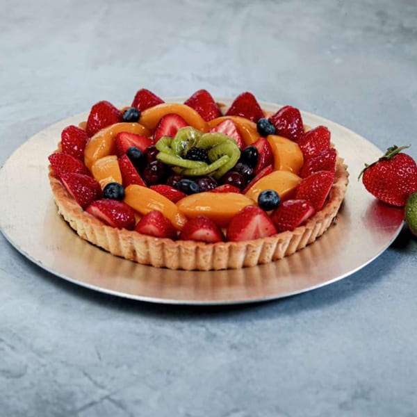 A vibrant fruit tart with strawberries, blueberries, peaches, and kiwi on a silver platter.