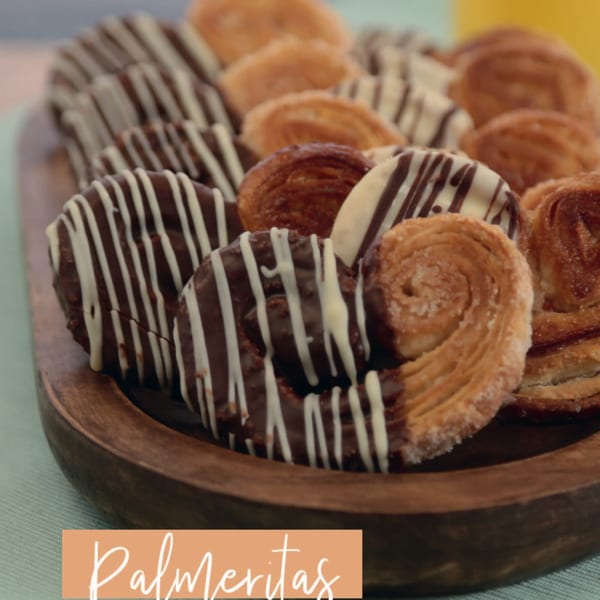 A wooden platter filled with palmeritas, some plain and some drizzled with chocolate and white icing.