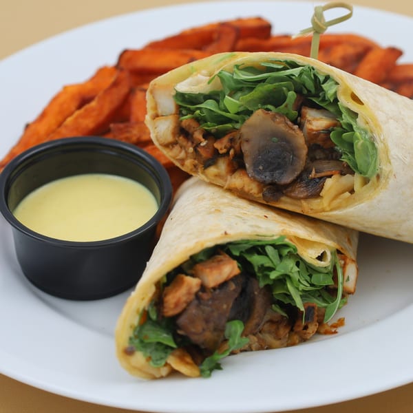 Two halves of a chicken and mushroom wrap with arugula, served with sweet potato fries and dipping sauce.