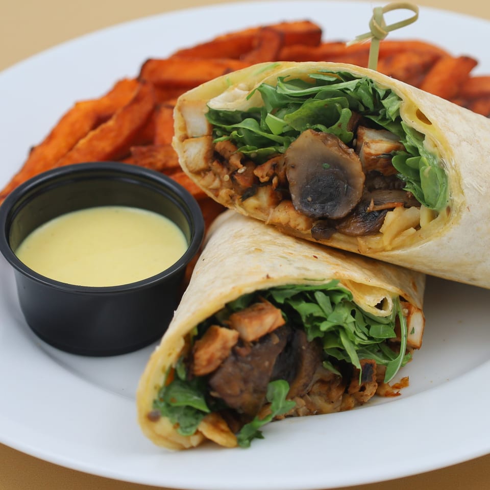 Two halves of a chicken and mushroom wrap with arugula, served with sweet potato fries and dipping sauce.