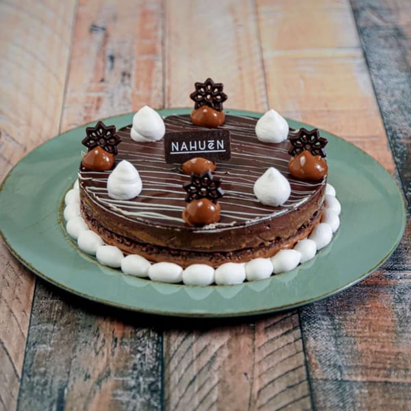 NAHUEN Gourmet Market's chocolate cake with dulce de leche, meringue, and chocolate decorations on a green plate.