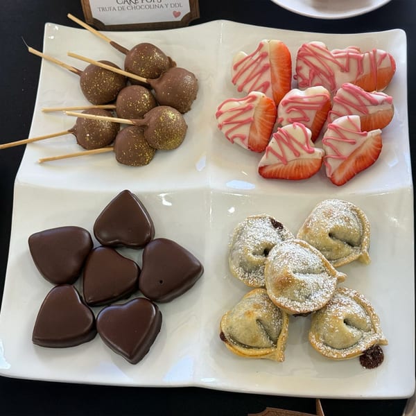 A white platter with chocolate cake pops, heart-shaped chocolate-covered strawberries, and mini empanadas.