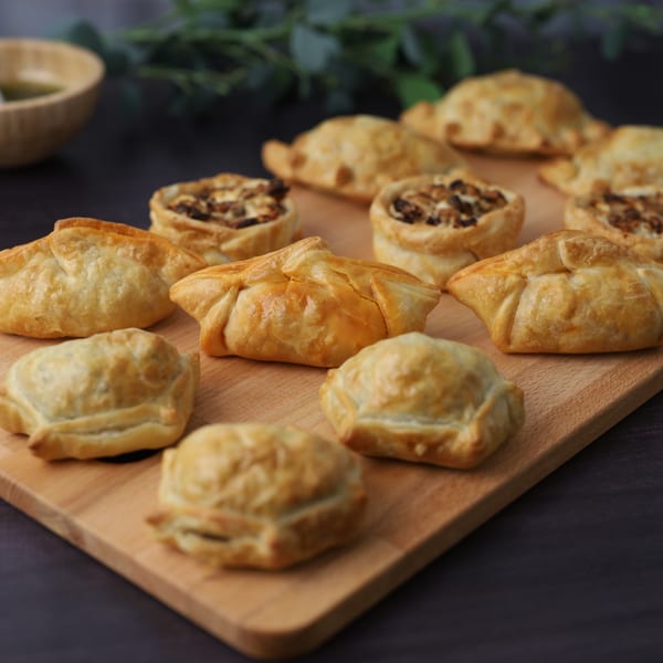 A wooden board filled with golden-brown Argentinian empanadas and savory tarts, ready to eat.