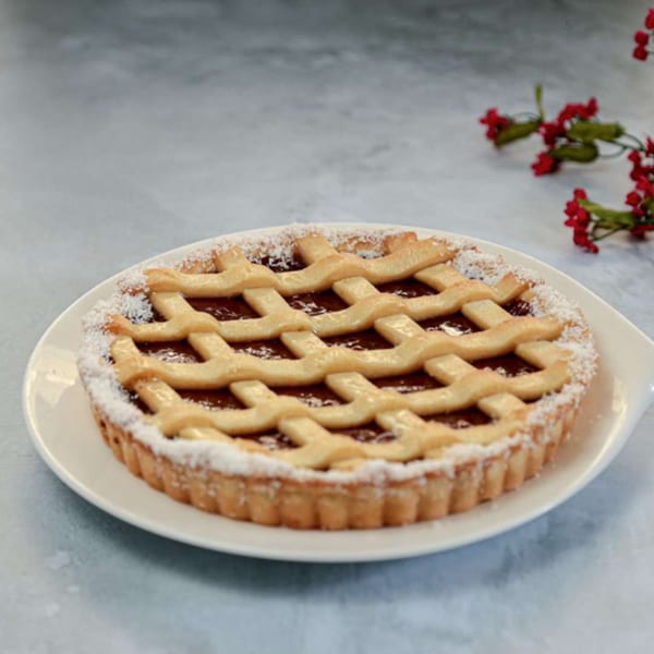 A round pastafrola tart with a lattice crust and dulce de leche filling, dusted with powdered sugar.