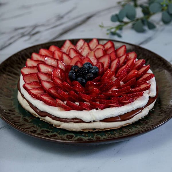 A strawberry and blueberry meringue cake with chocolate filling on a dark plate.