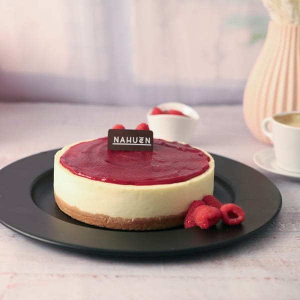 NAHUEN Gourmet Market cheesecake with raspberry topping and fresh raspberries on a black plate.