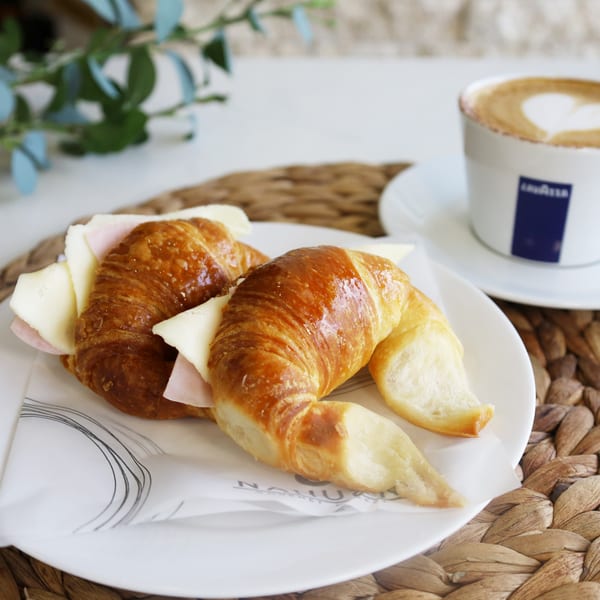 Two golden croissants filled with ham and cheese, alongside a latte with a heart design.