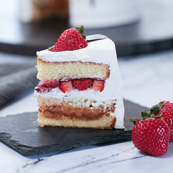 Slice of strawberry shortcake with dulce de leche filling on a black slate board.