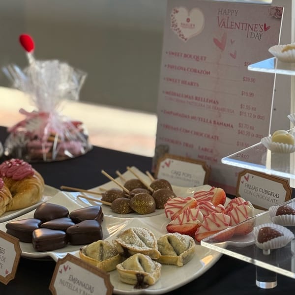 A Valentine's Day dessert display with chocolate-covered strawberries, heart-shaped chocolates, and mini empanadas.
