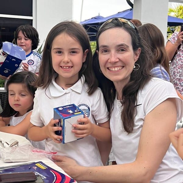 A smiling woman and young girl, both with dark hair, pose for a photo at an outdoor event.