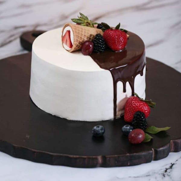 A white cake with chocolate ganache, topped with strawberries, blackberries, grapes, and a waffle cone.