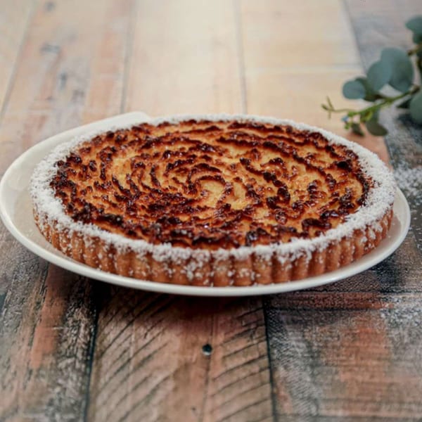 A golden brown Argentinian coconut tart, dusted with powdered sugar, on a white plate.