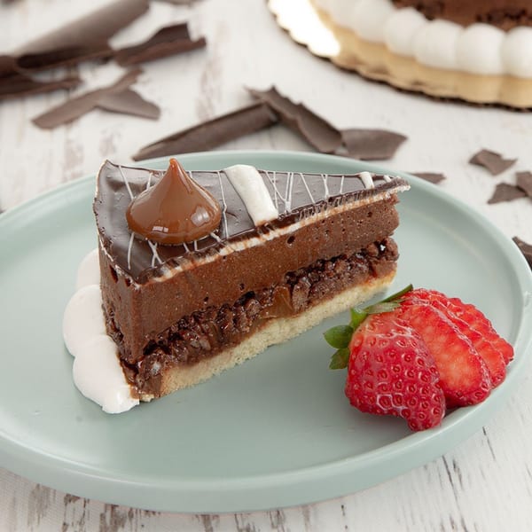 A slice of chocolate cake with dulce de leche, whipped cream, and sliced strawberries on a plate.