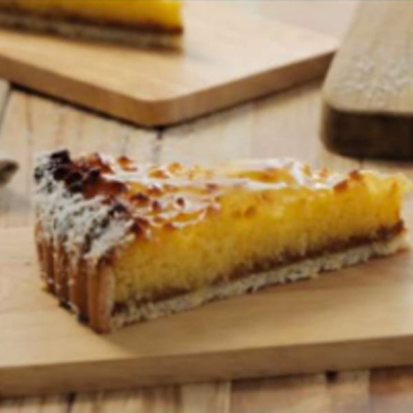 A slice of Argentinian lemon tart with a golden crust and powdered sugar on a wooden board.