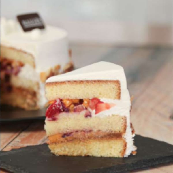 A slice of Nahuen Gourmet Market's fruit cake with white frosting and a whole cake in the background.