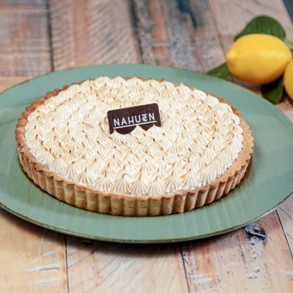 A Nahuen lemon meringue pie with toasted peaks on a green plate, with lemons in the background.