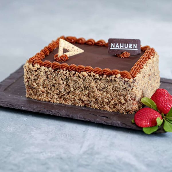 Square Nahuen chocolate cake with nut-covered sides, dulce de leche piping, and fresh strawberries.