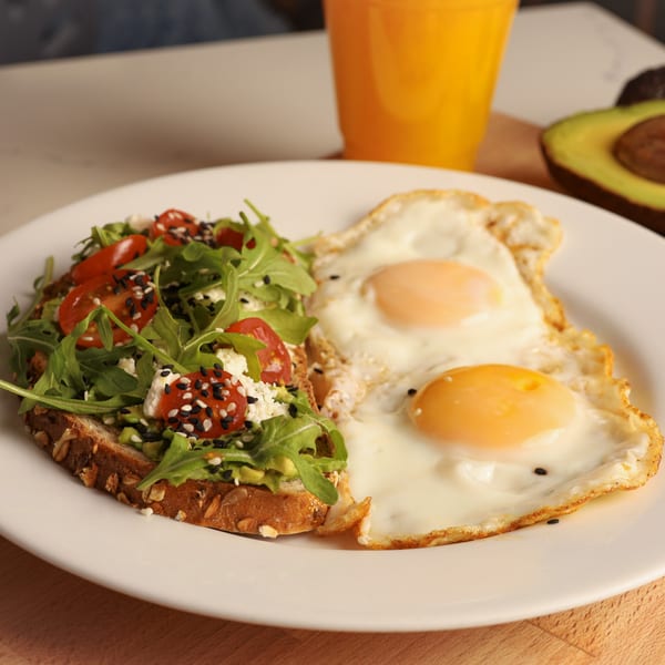 Avocado toast with cherry tomatoes, feta, arugula, sesame seeds, and two fried eggs.