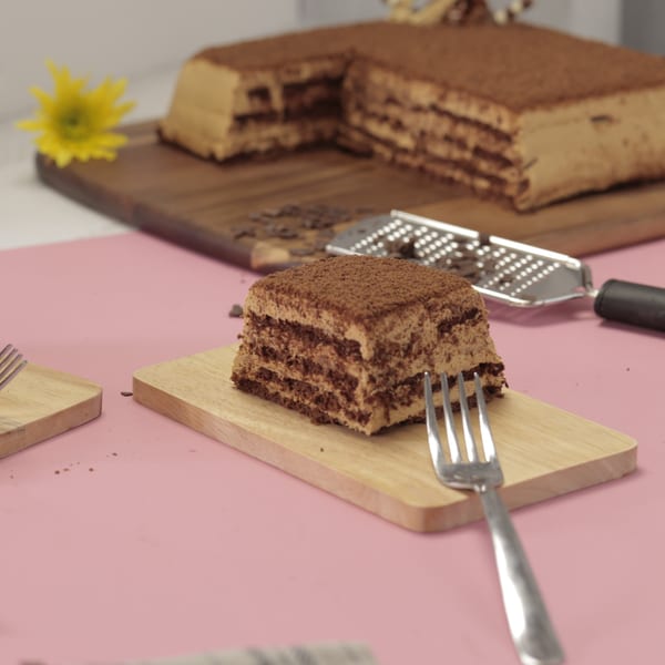 A slice of layered chocolate cake with cocoa powder on a wooden board with a fork.