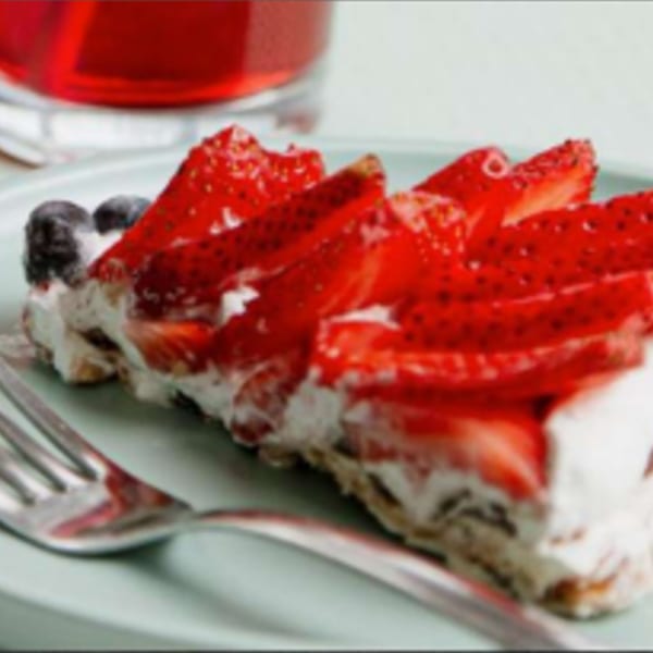 A slice of strawberry tart with whipped cream and blueberries on a light blue plate.