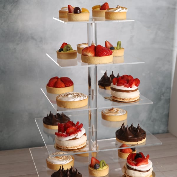 A tiered display stand showcases various fruit tarts, meringue tarts, and chocolate tarts.