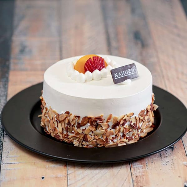 NAHUEN Gourmet Market cake with white frosting, sliced almonds, and fruit on a black plate.