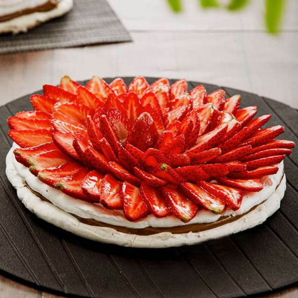 A strawberry meringue cake with dulce de leche filling on a black serving plate.