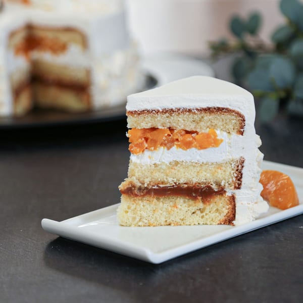 A slice of Nahuen Gourmet Market's layered cake with white frosting, orange filling, and dulce de leche.