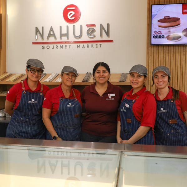 Five smiling NAHUEN Gourmet Market employees in red shirts and striped aprons stand behind a counter.