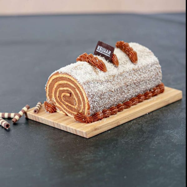 A Nahuen chocolate swiss roll cake, dusted with coconut flakes and dulce de leche frosting.