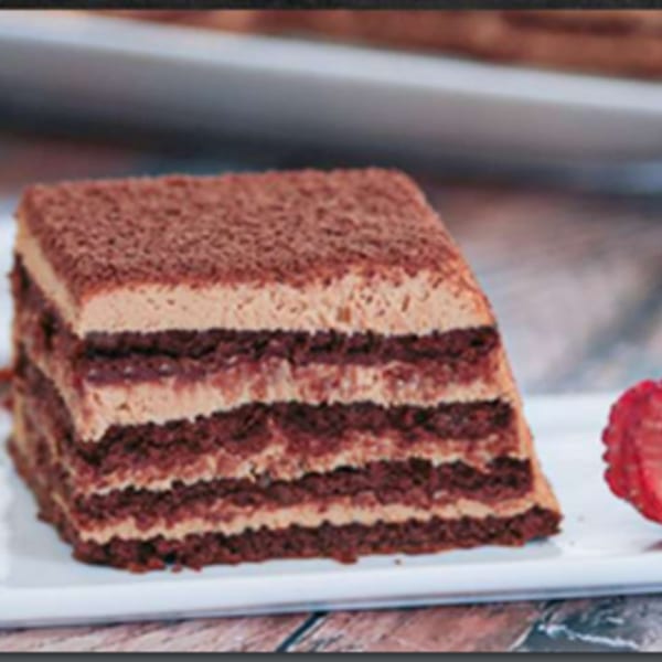 Layered chocolate cake with light brown frosting and cocoa powder, garnished with a strawberry slice.