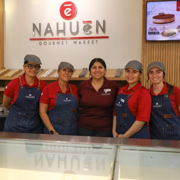 Five smiling NAHUEN Gourmet Market employees in red shirts and aprons stand behind a counter.