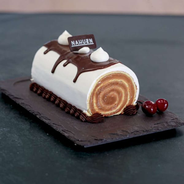 Nahuen Gourmet Market's dulce de leche swiss roll cake with white frosting, chocolate drizzle, and cherries.