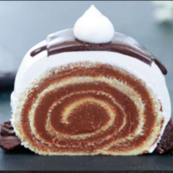 A slice of chocolate and vanilla swiss roll cake with chocolate drizzle and whipped cream.